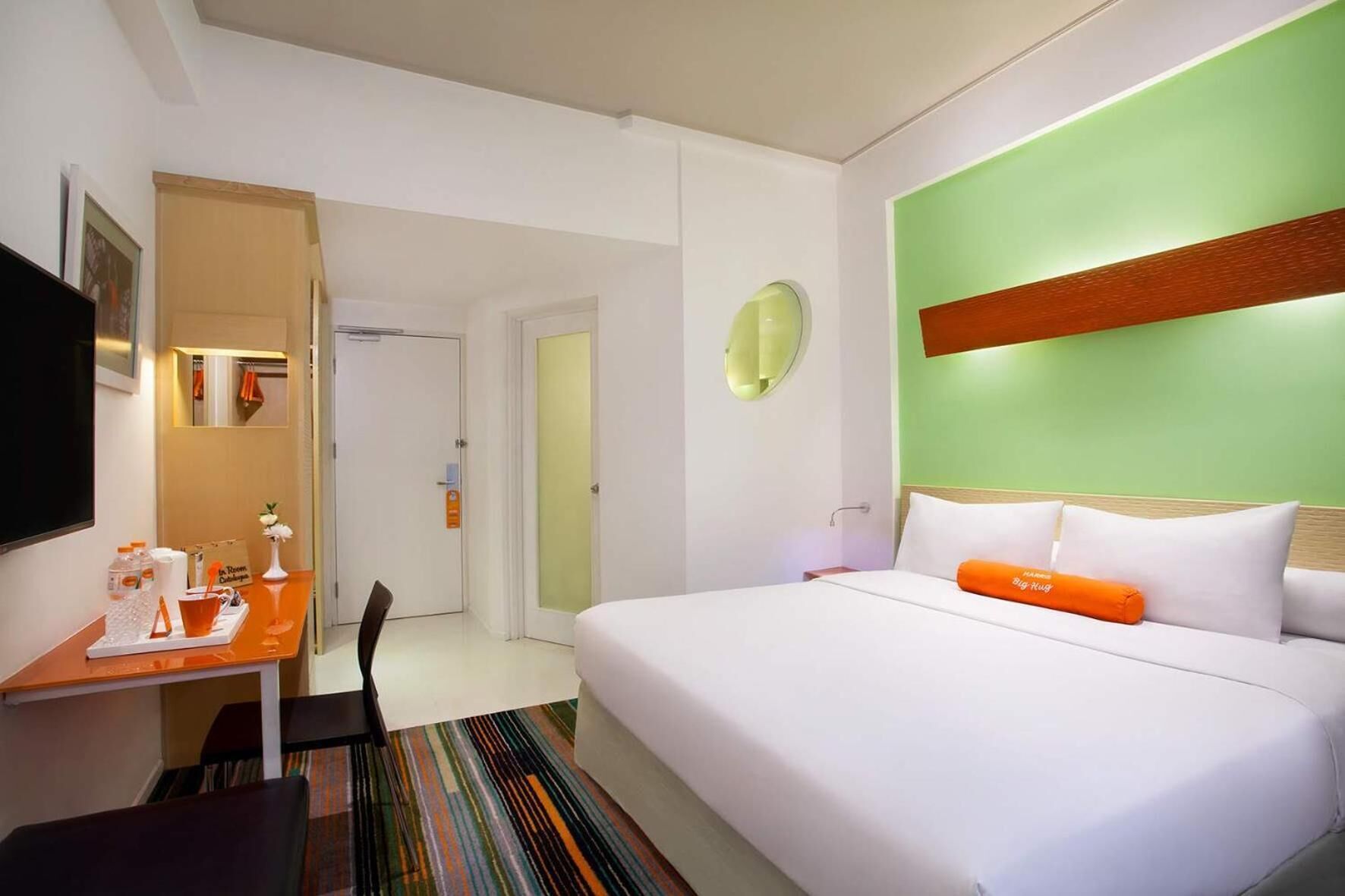 Une chambre d’hôtel comprenant un lit, un bureau avec une chaise, un miroir et un téléviseur.
