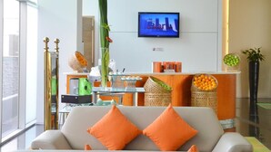 Un salon moderne avec un canapé, des coussins orange, un téléviseur et une plante décorative.
