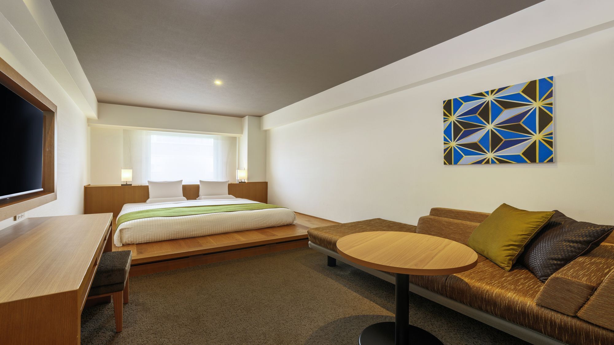 Ein modernes Hotelzimmer mit Bett, Sofa, kleinem Tisch und Fernseher.