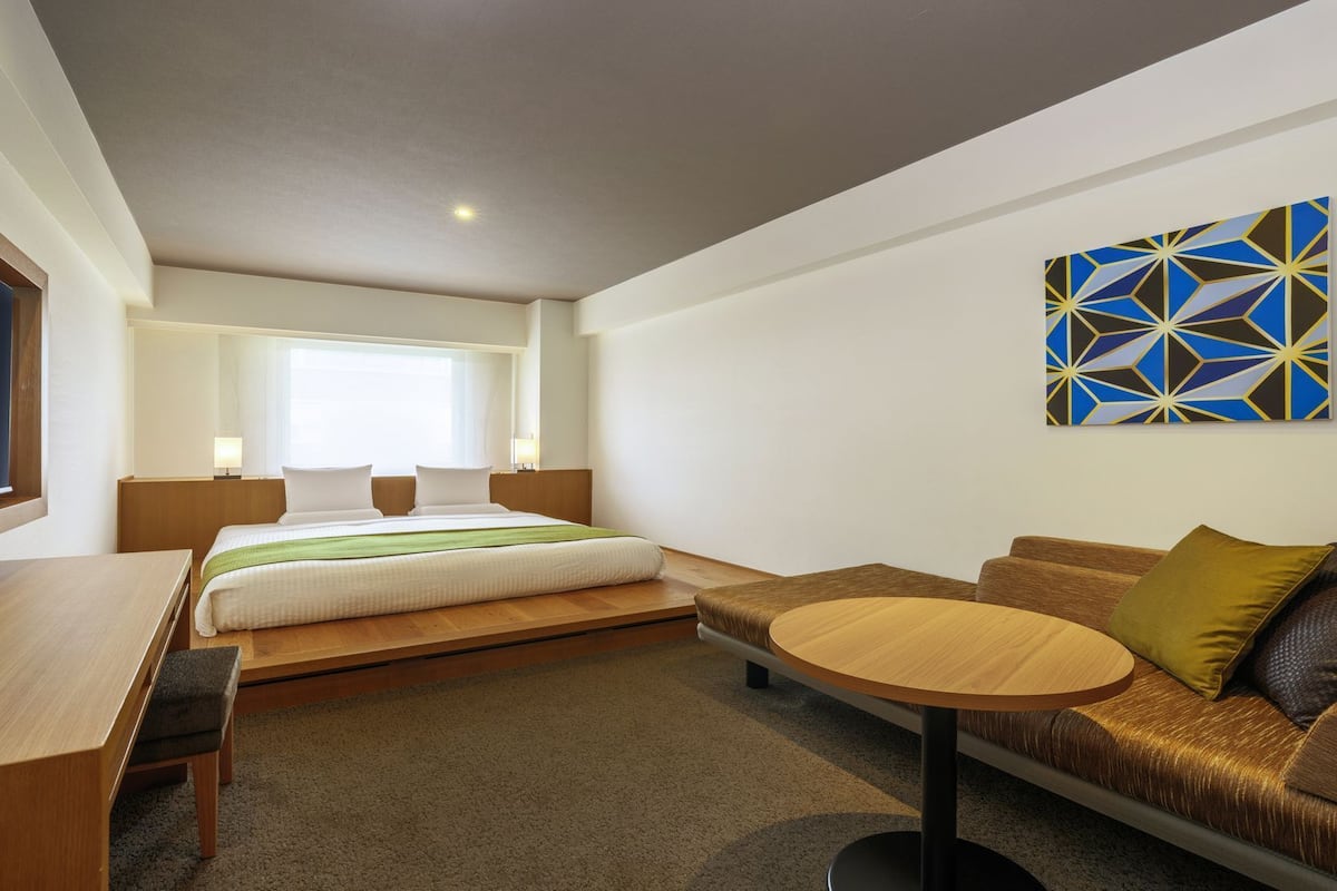 A modern hotel room with a bed, a sofa, a small table, and a TV.