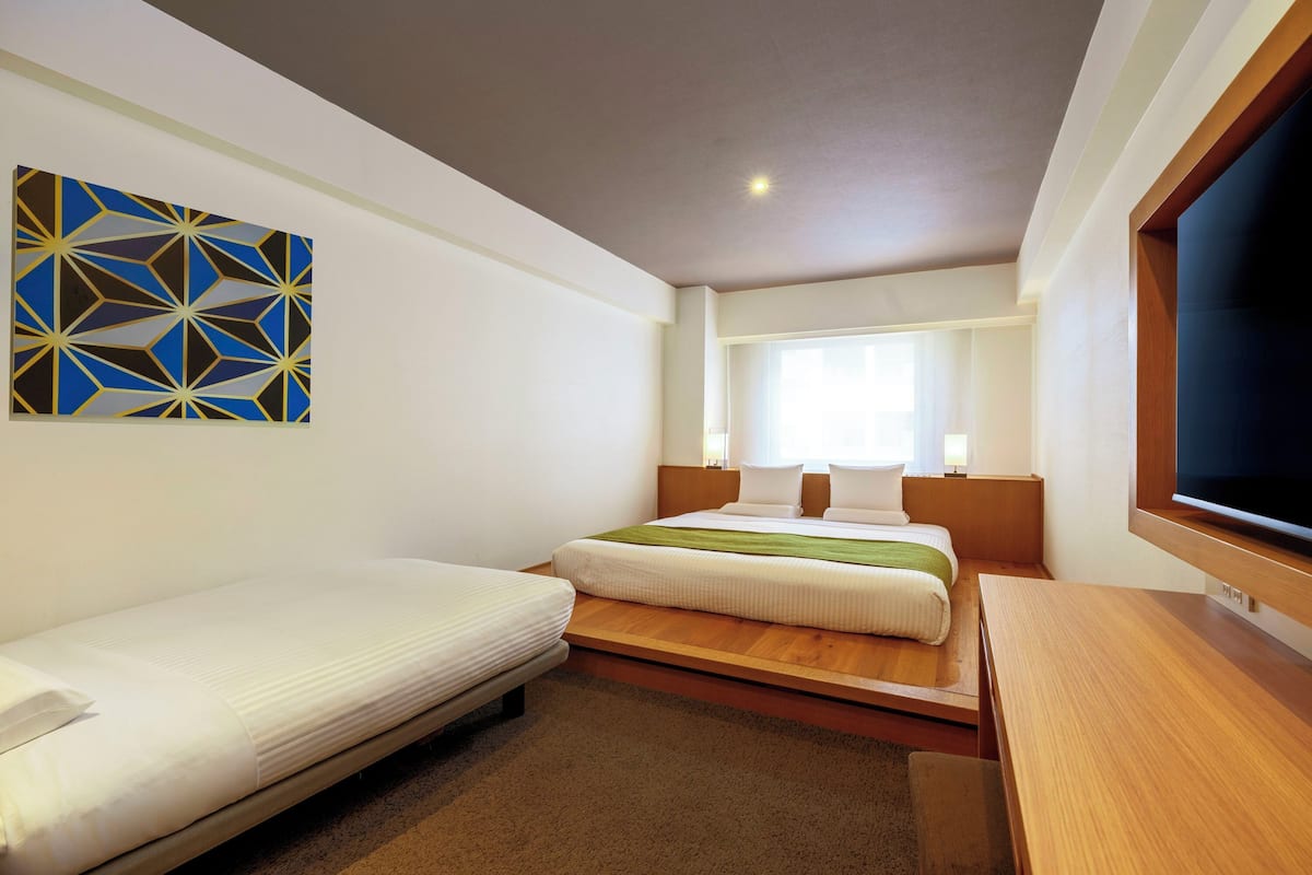A hotel room with two beds, a wooden desk, a television, and a geometric wall art piece.