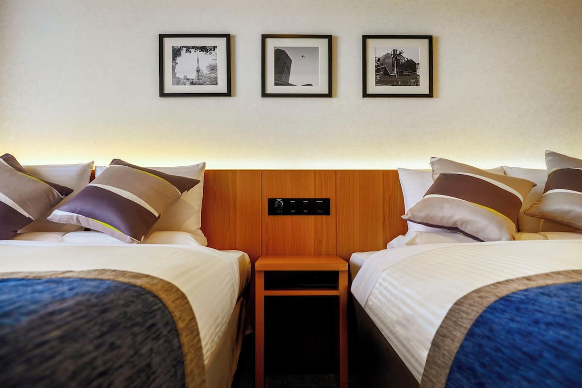 A hotel room with two beds, a nightstand, and three framed pictures on the wall.