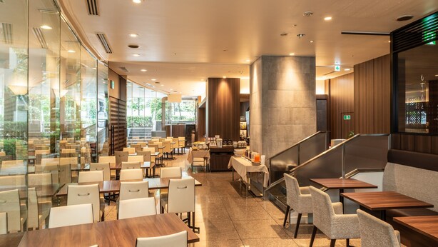 A modern dining area with glass partitions, multiple seating arrangements, and a staircase leading to an upper level.