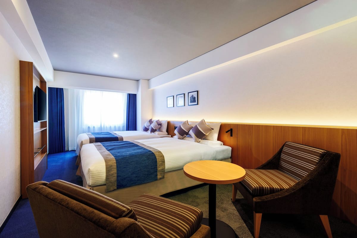 A hotel room with a large bed, two bedside tables, a small round table, a sofa, and a TV.