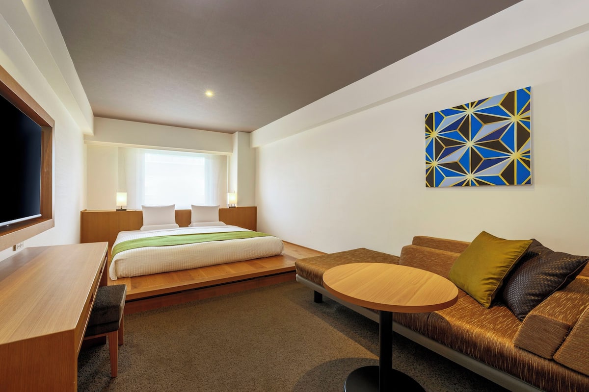A modern hotel room with a bed, a sofa, a round table, and a TV.