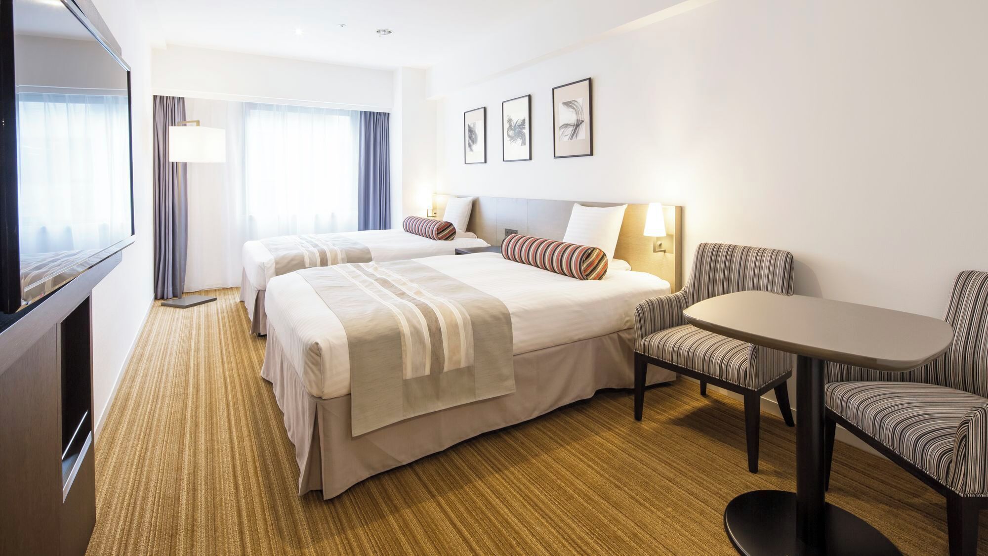 Ein Hotelzimmer mit zwei Betten, einem Fernseher, einem Schreibtisch und einem Sessel.
