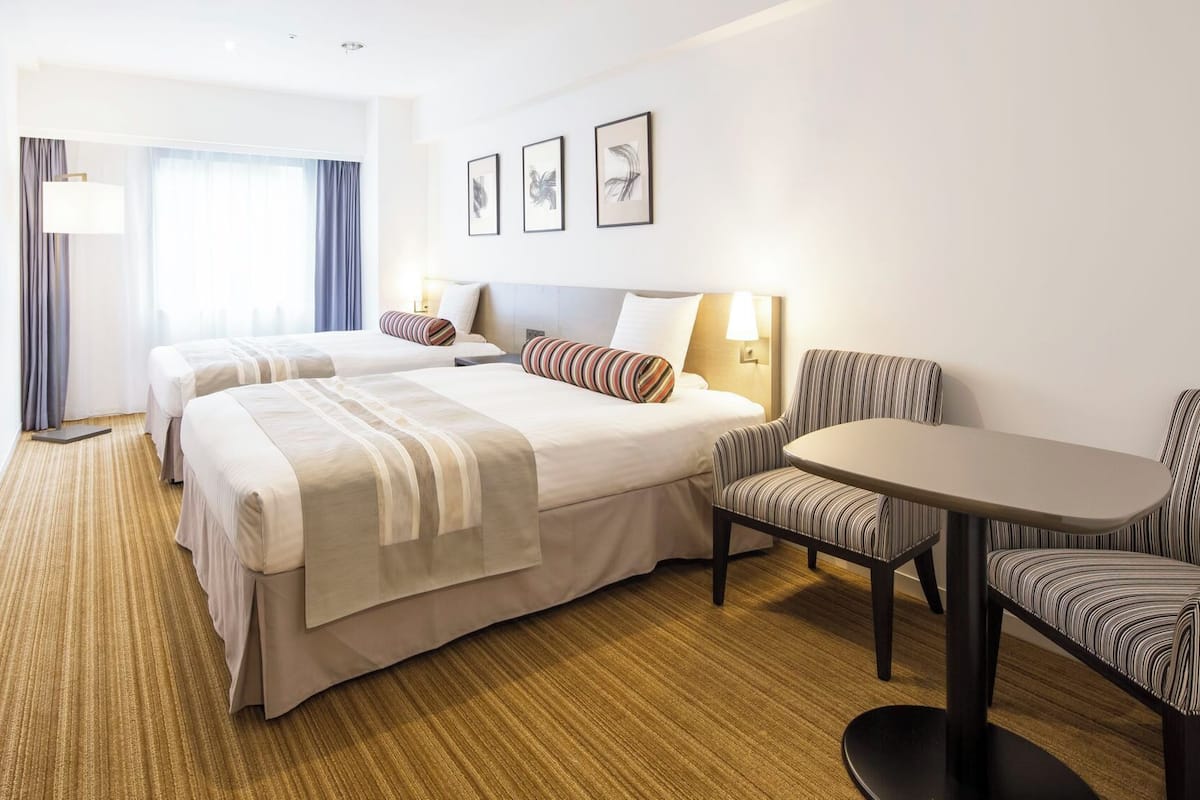 A hotel room with two beds, a TV, a desk, and a chair.