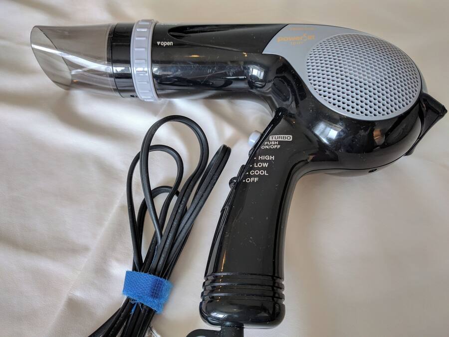 A hair dryer with a clear nozzle, a black handle, and a cord with a blue tie.