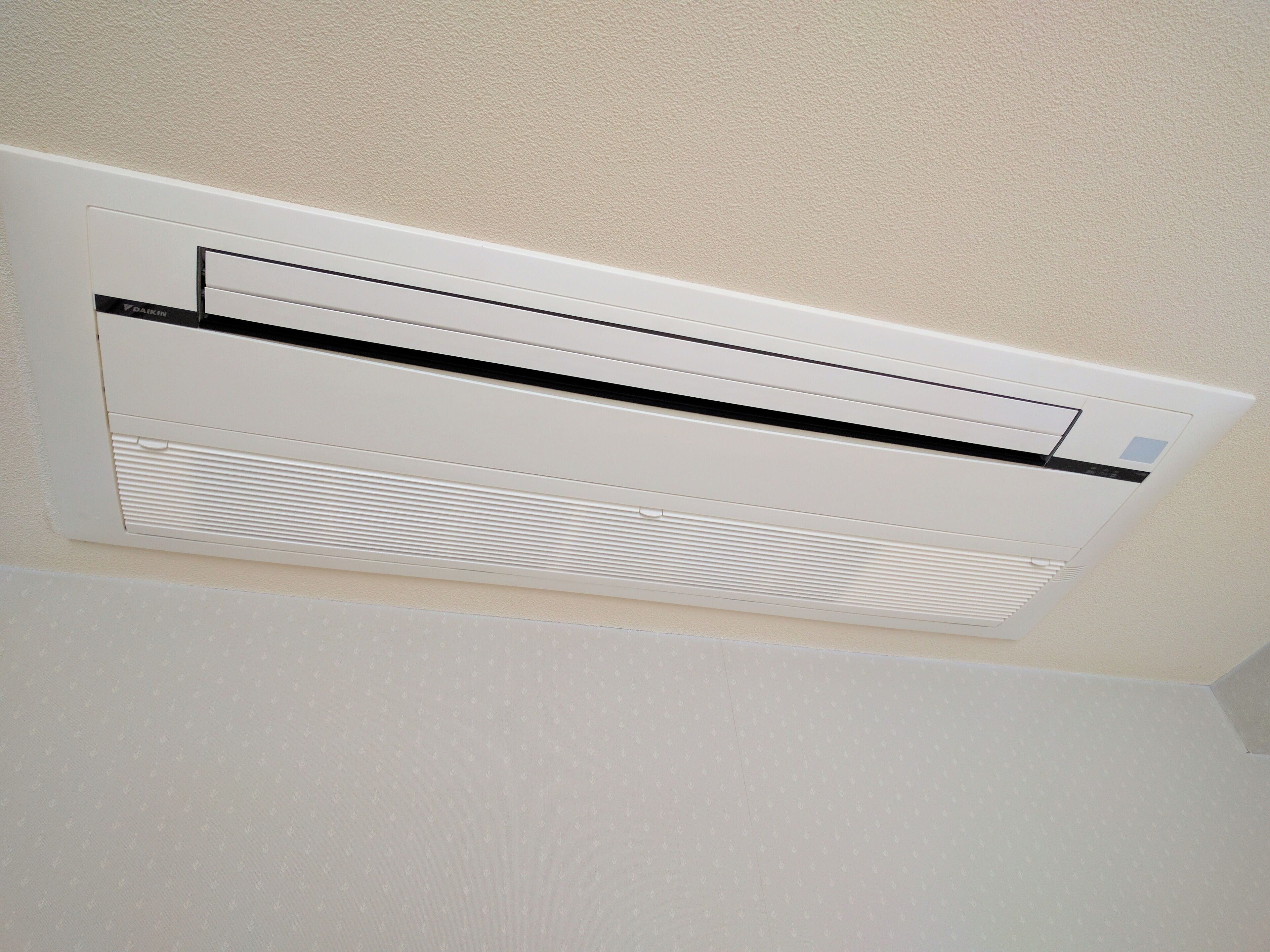 Un appareil de climatisation mural blanc, doté d’un panneau de commande et d’une grille d’aération.