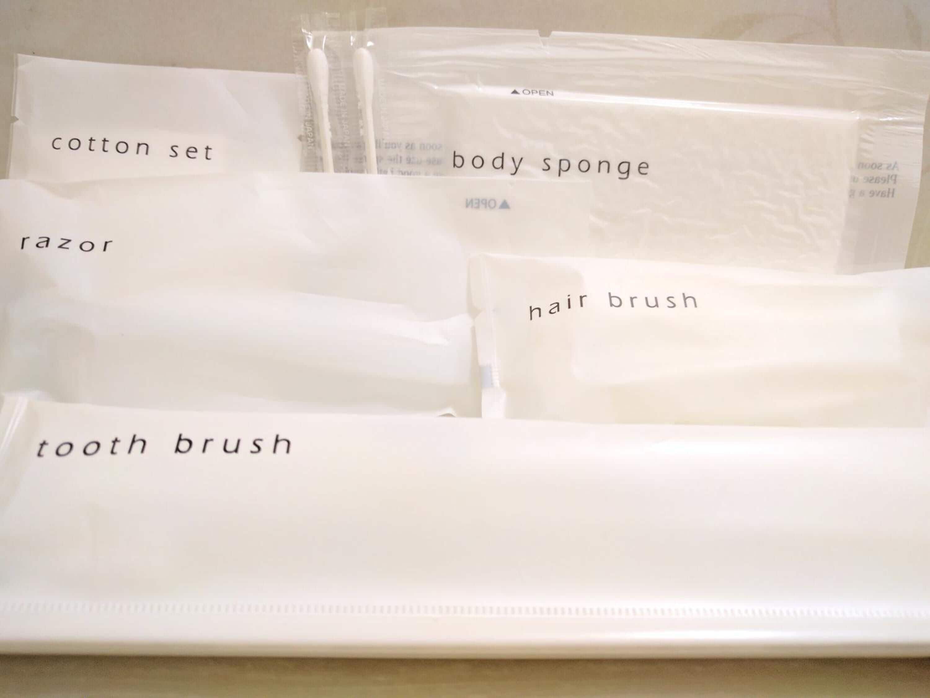 Un juego de artículos de tocador blanco que incluye un set de algodón, esponja de baño, afeitadora, cepillo para el cabello y cepillo de dientes.