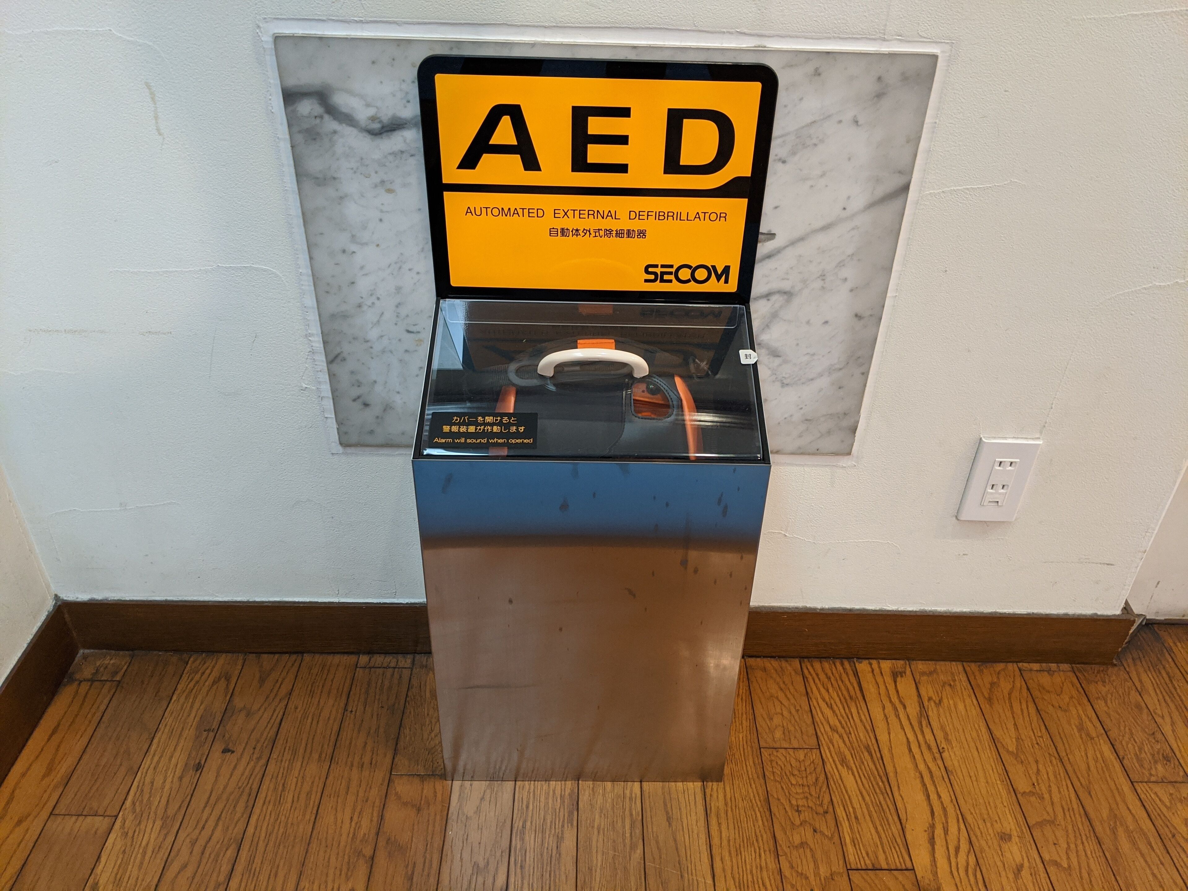 An AED device mounted on a wall with a marble-like texture.