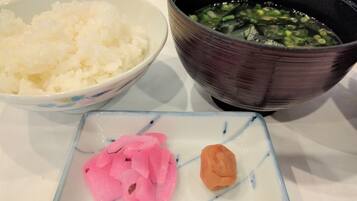 A bowl of white rice, a bowl of green vegetable soup, and a small dish with pink pickled vegetables and a piece of orange food on a table.