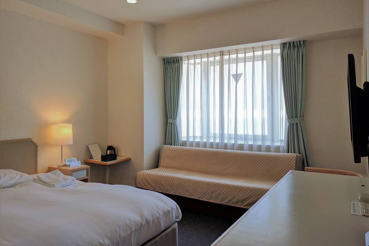 Une chambre d’hôtel avec deux lits, un bureau, une lampe, une chaise et une fenêtre avec des rideaux.