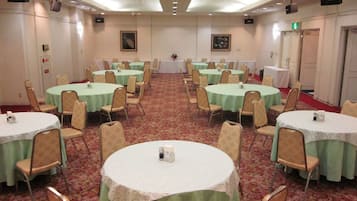 A conference room with multiple round tables covered with green tablecloths, beige chairs, and a carpeted floor.