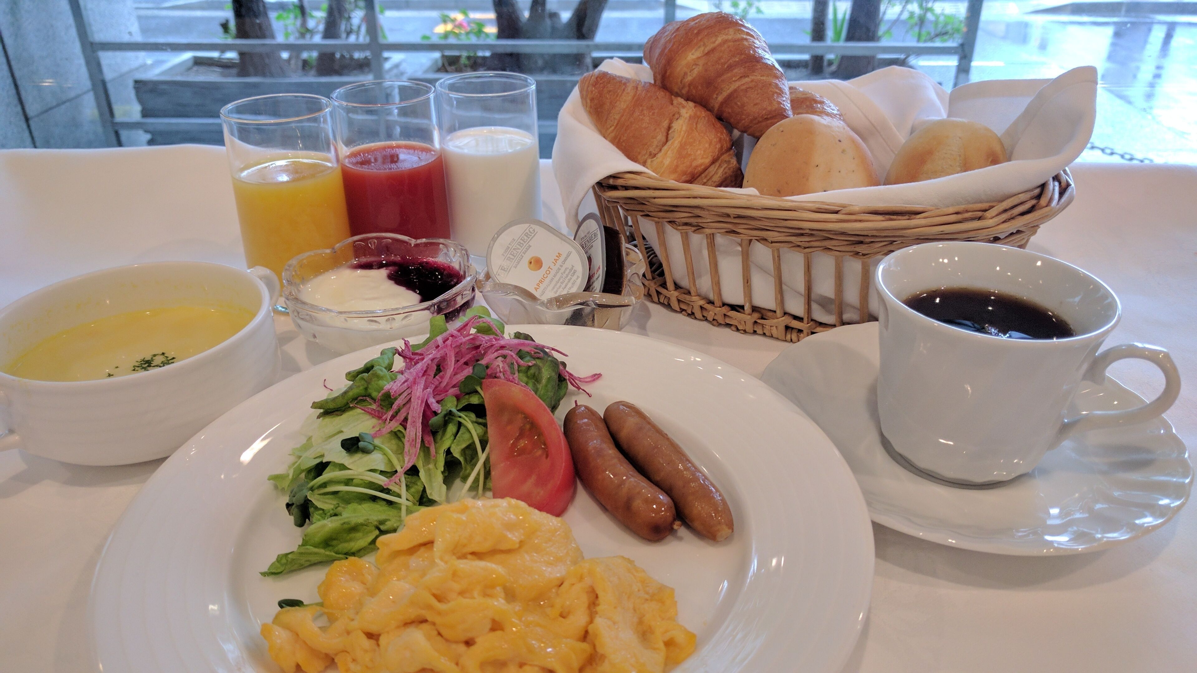 En morgenmadsopsætning med røræg, pølser, en salat, croissanter og drikkevarer.