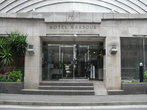 La entrada al Hotel Harbour en Yokosuka, con una fachada moderna de vidrio y una base de piedra.