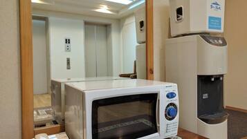 A microwave oven with a control panel, a water dispenser, and a telephone on a wooden table.