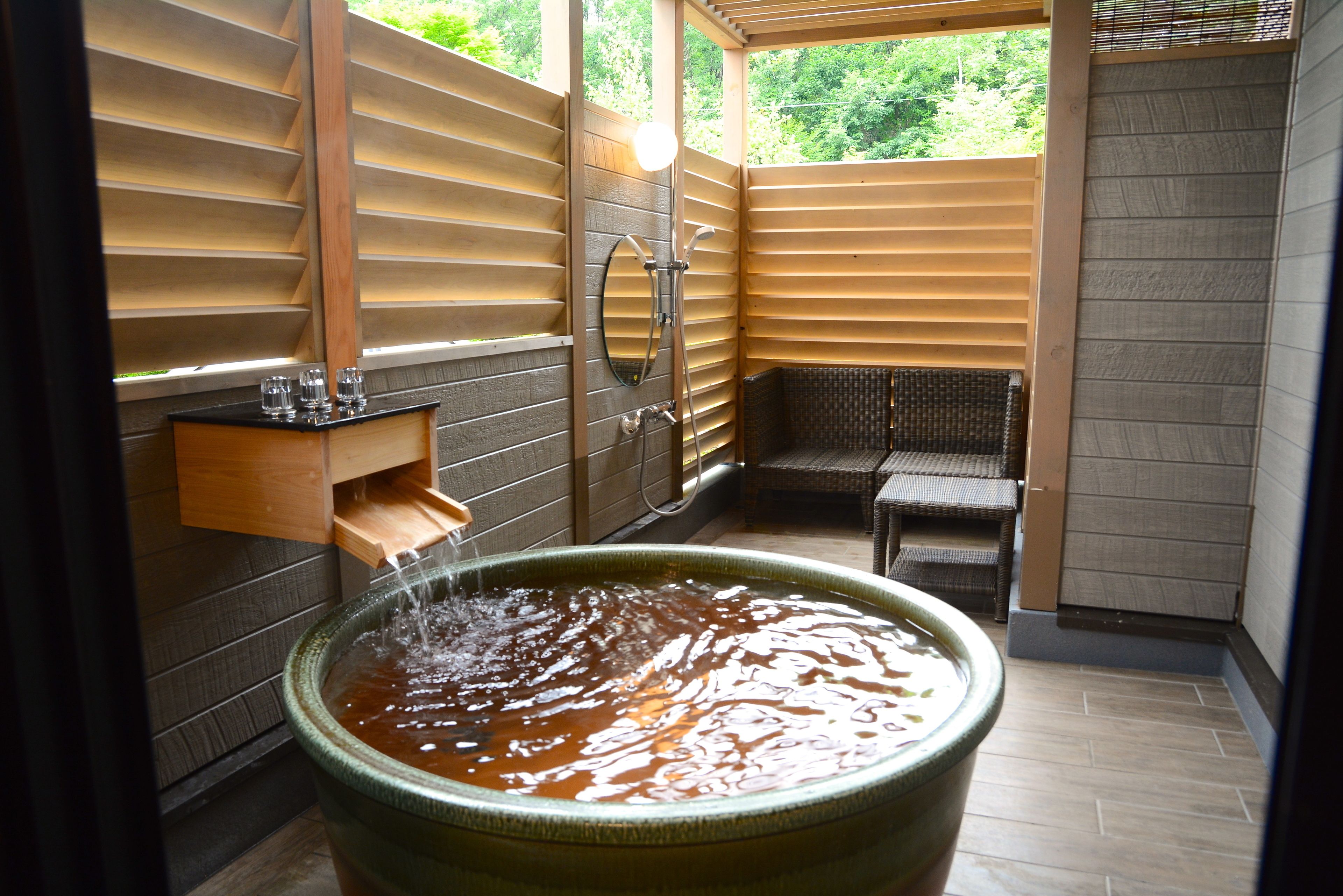 A traditional Japanese onsen with a large stone hot tub, wooden sliding doors, and a small seating area.