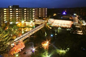 Un hotel de varios pisos con una galería techada y un edificio grande con una estructura iluminada en azul al fondo.