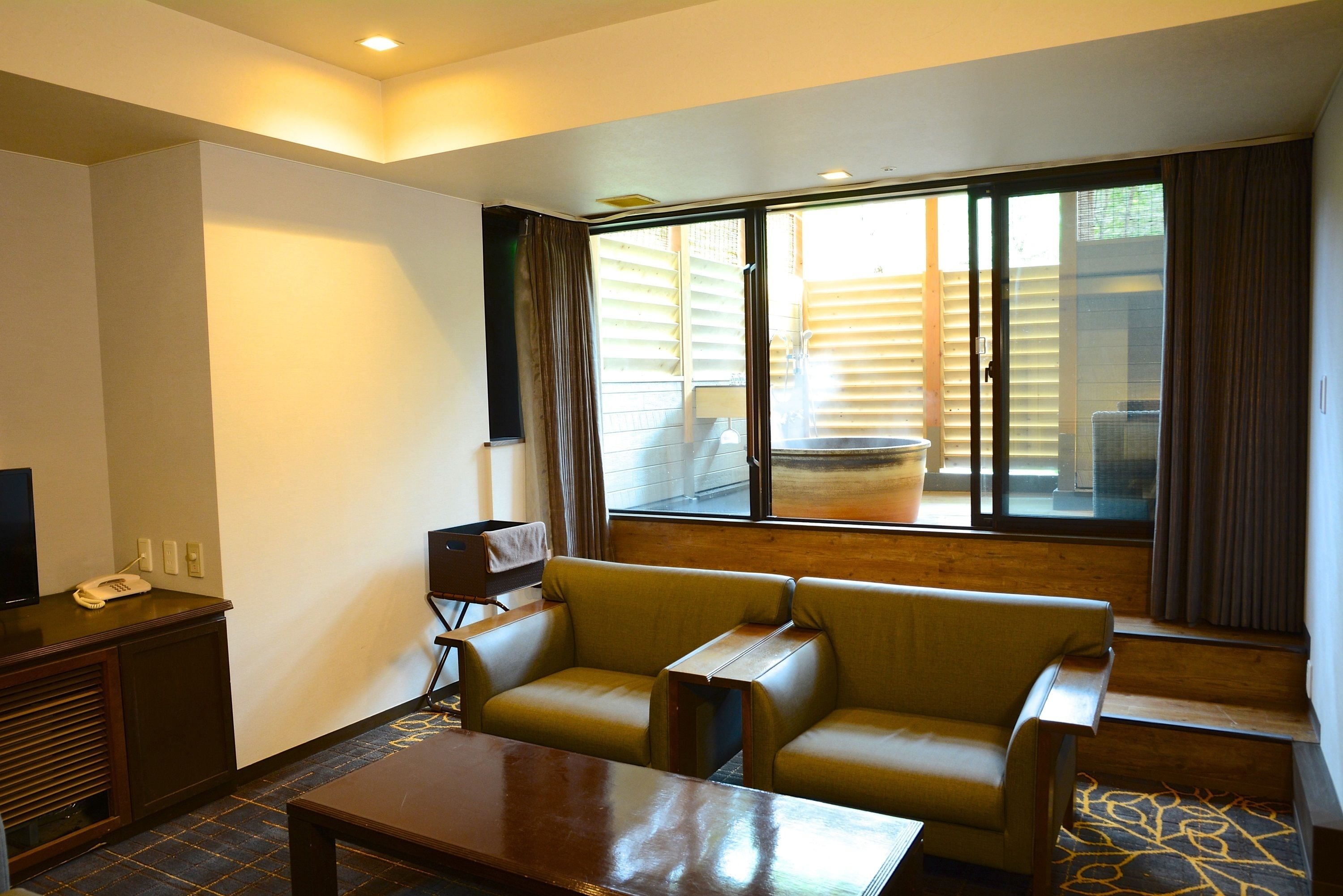 Una habitación de hotel con sofá, mesa de centro, televisor y ventana con persianas.