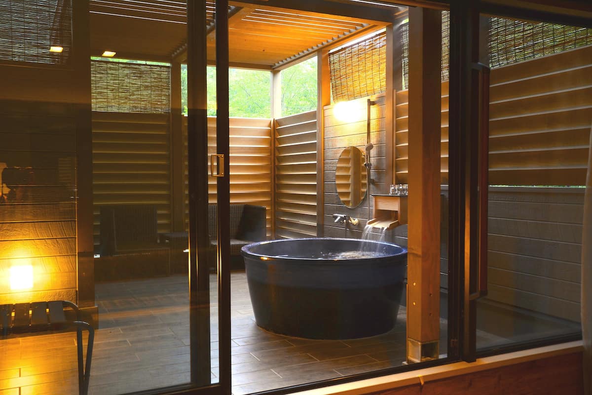 Een moderne badkamer met een groot bad, een douchecabine met glazen wanden en een houten buitenmuur.