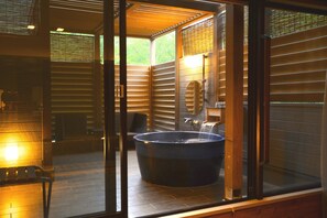 Un baño moderno con una bañera grande, una zona de ducha con paredes de cristal y una pared exterior de madera.