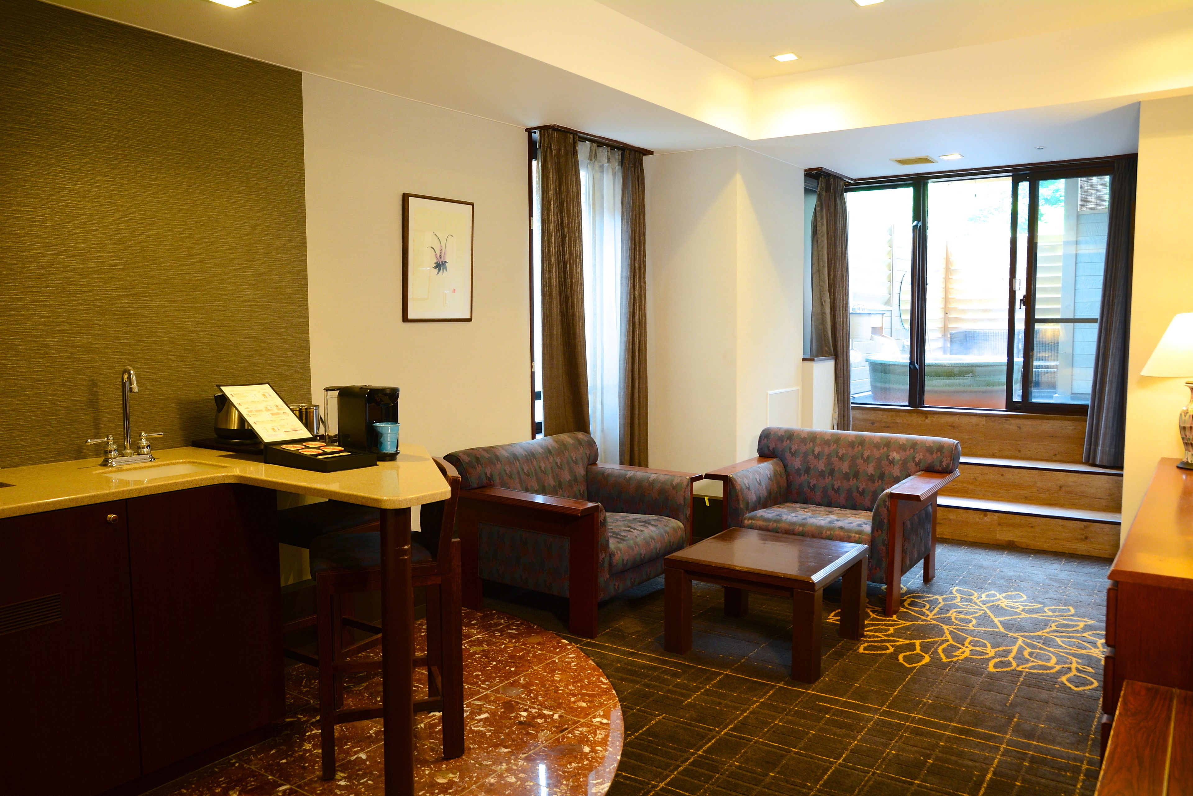 A hotel room with a dining area, a sofa, a small table, and a view of the outdoors through a sliding door.