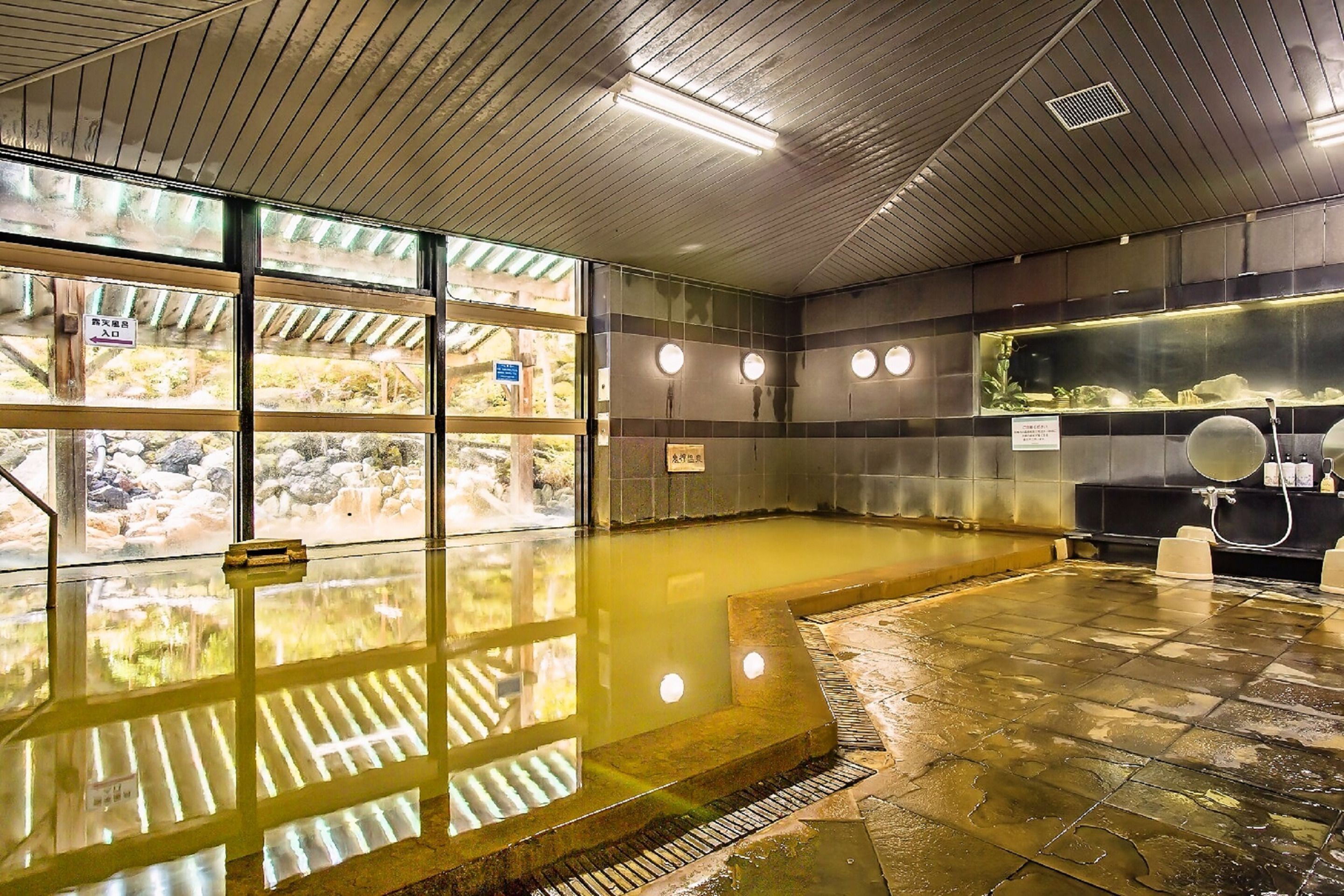 Un onsen japonais traditionnel avec un sol en pierre, un plafond en bois et de grandes fenêtres.