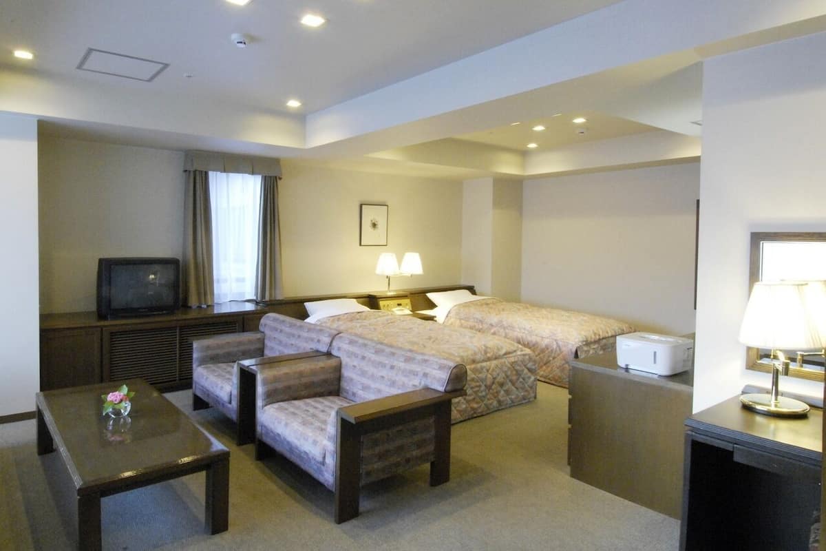 Une chambre d’hôtel avec un lit, deux canapés, une télévision, un bureau et une lampe.