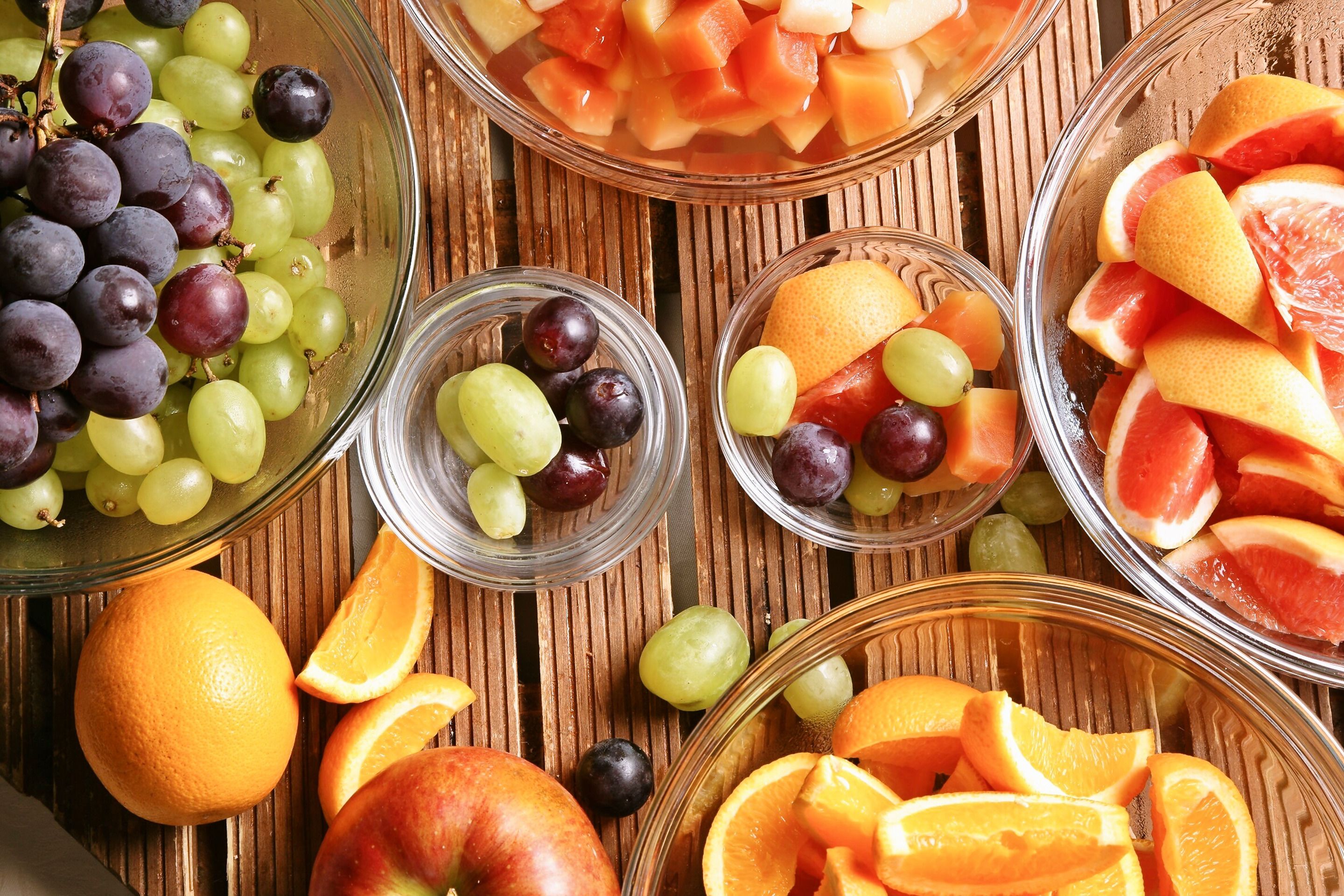 A variety of fruits including grapes, oranges, and melon slices arranged on a wooden surface.
