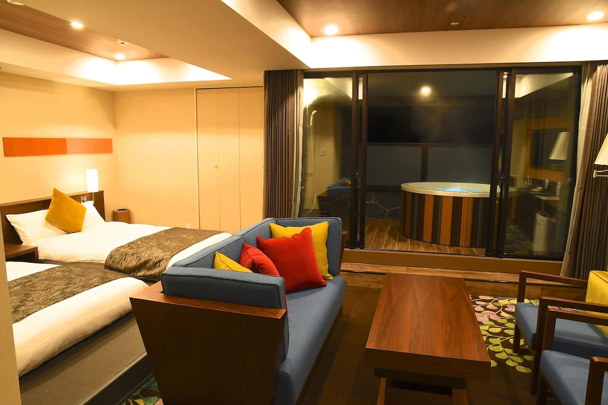 Een hotelkamer met een bed, een slaapbank, een eettafel en een balkon met een tafel en stoelen.