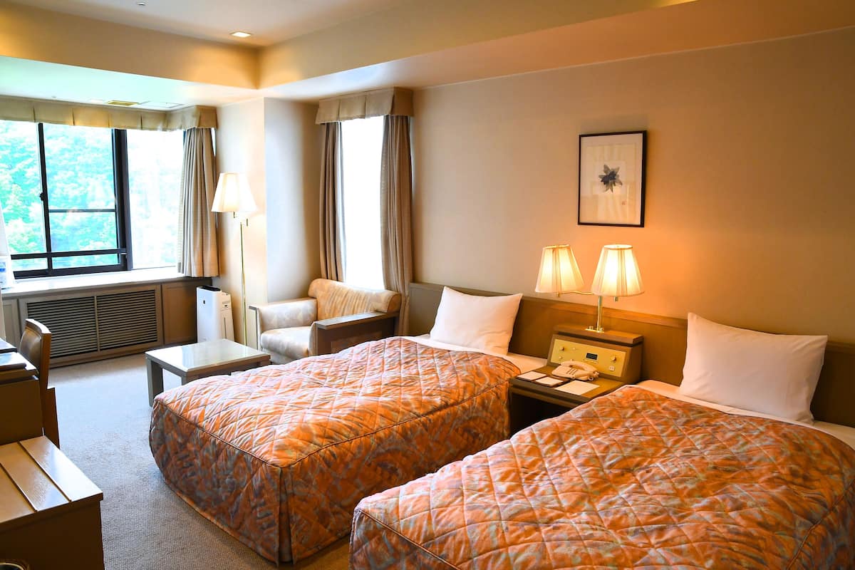 Een hotelkamer met twee bedden, een bureau, een stoel, een lamp en een raam met gordijnen.