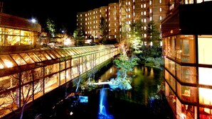 A nighttime view of a building with illuminated windows and a bridge over a water feature. - Karuizawa Club Hotel Karuizawa 1130 / Hewitt Resort (Tsumagoi)