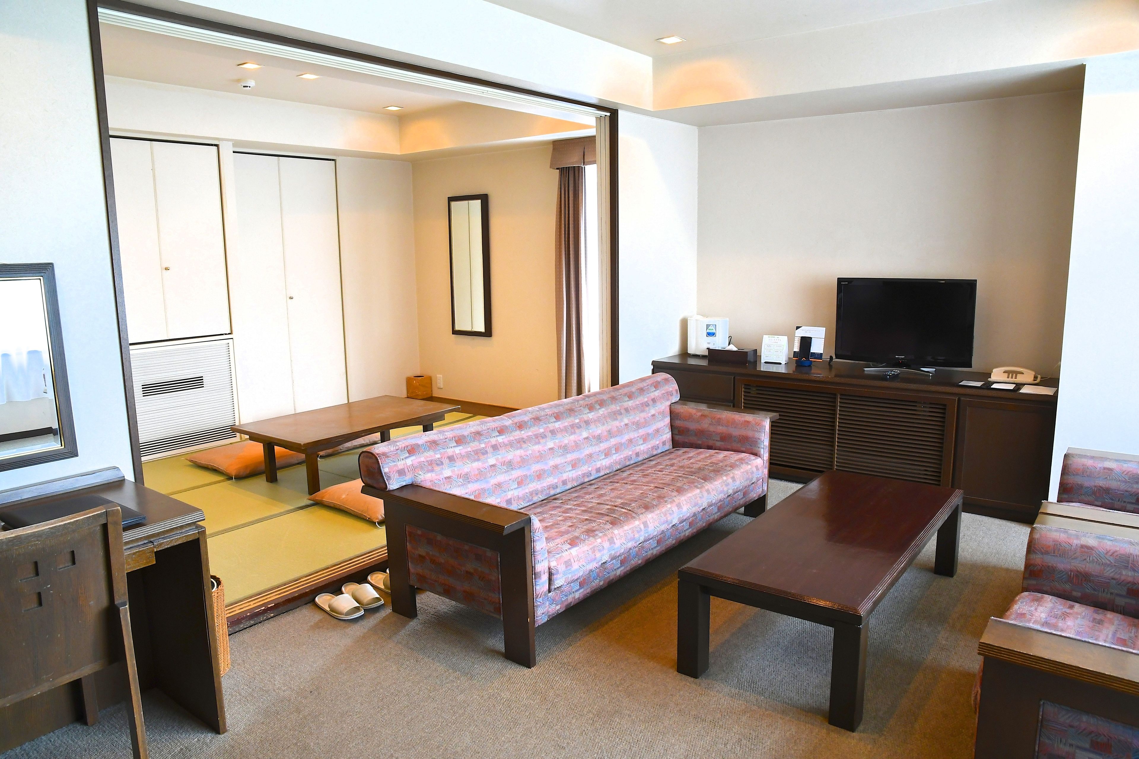 A hotel room with tatami mats, a sofa, a TV, and a desk.