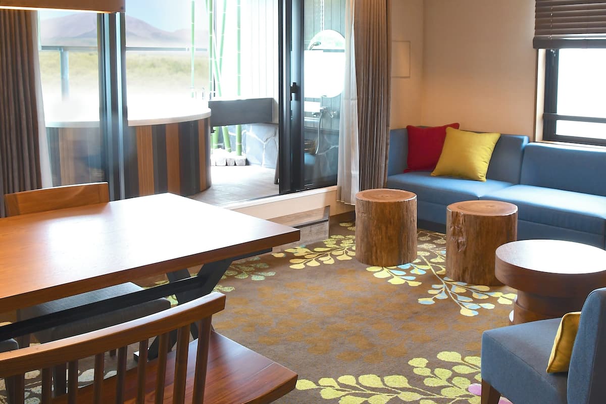 Een moderne zithoek met een eettafel, houten stoelen, een blauwe bank met kussens en een kamerbreed tapijt.