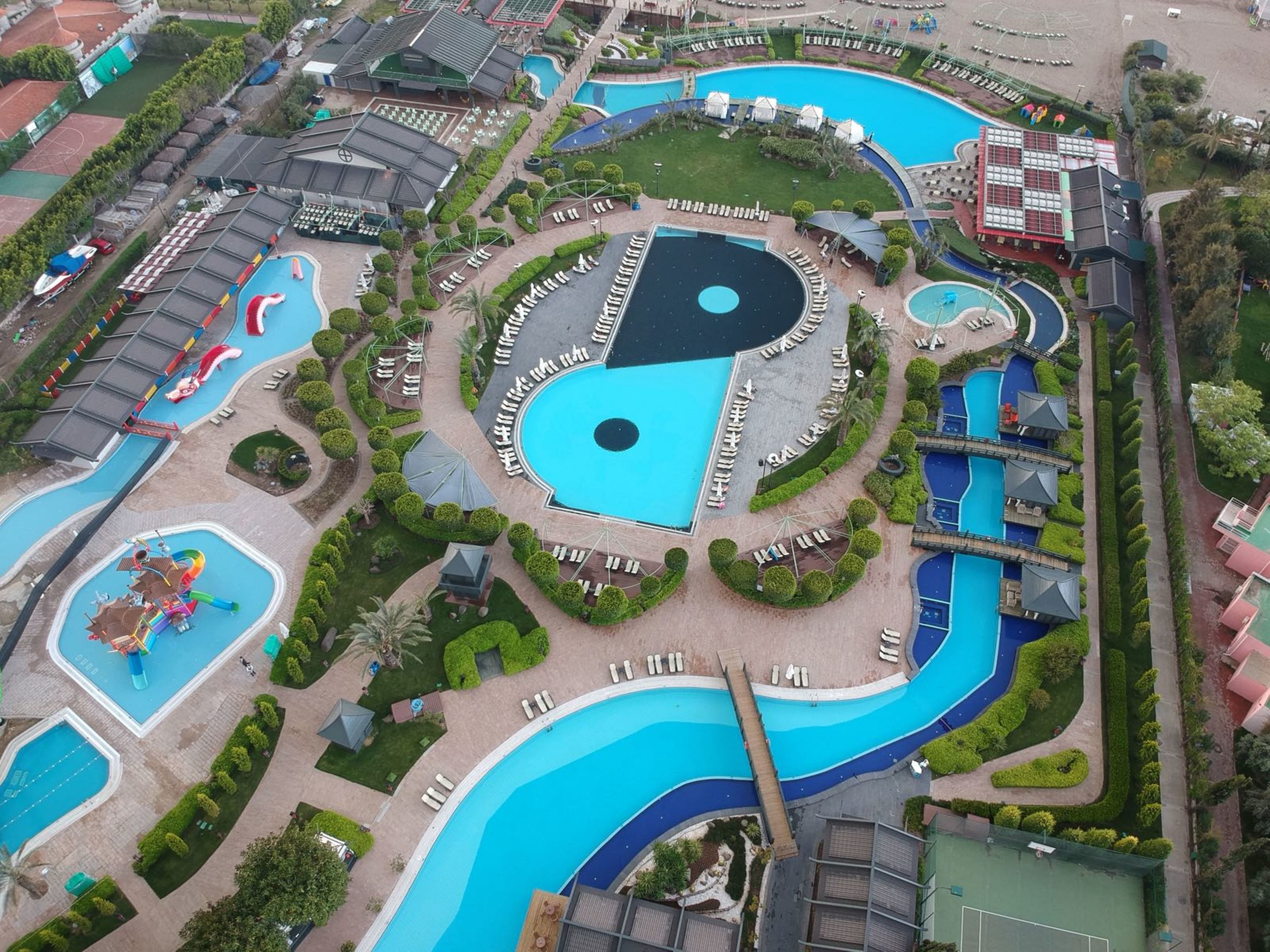 Vista aérea de un parque temático con múltiples piscinas, toboganes acuáticos y una piscina central de diseño singular.