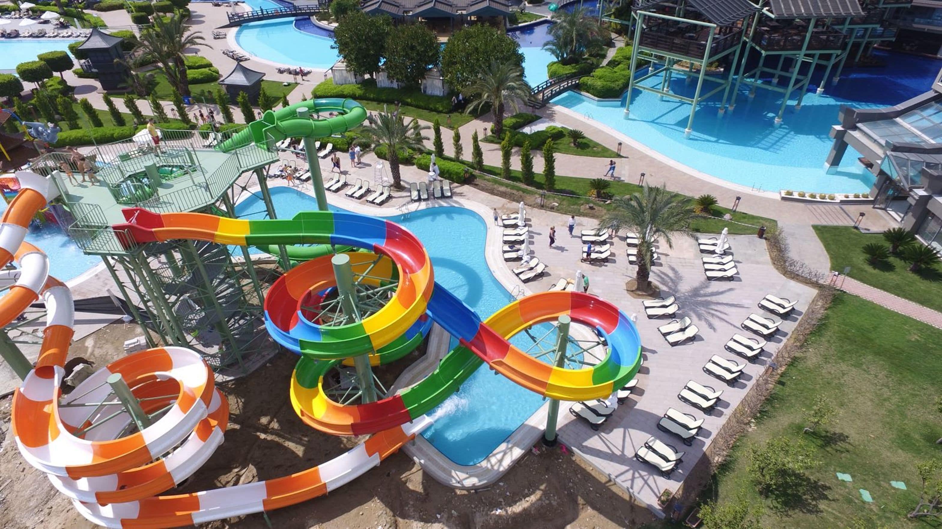 Un parque acuático con toboganes y piscinas, rodeado de sillas de descanso y palmeras.
