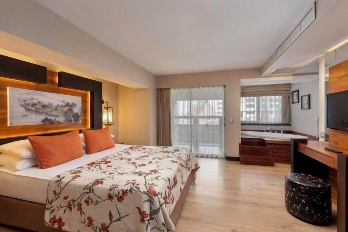 A hotel room with a bed, a desk, a television, and a window with curtains.
