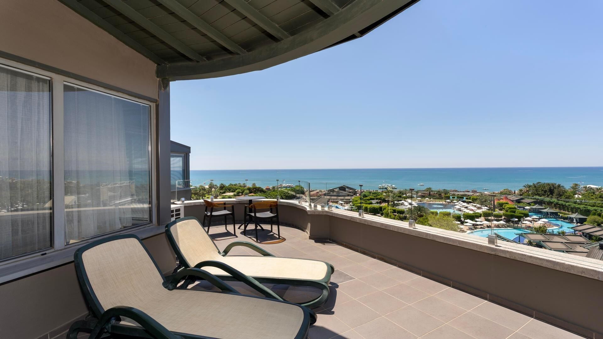 Ein Balkon mit zwei Liegestühlen, Blick aufs Meer und ein Resort-Poolbereich.