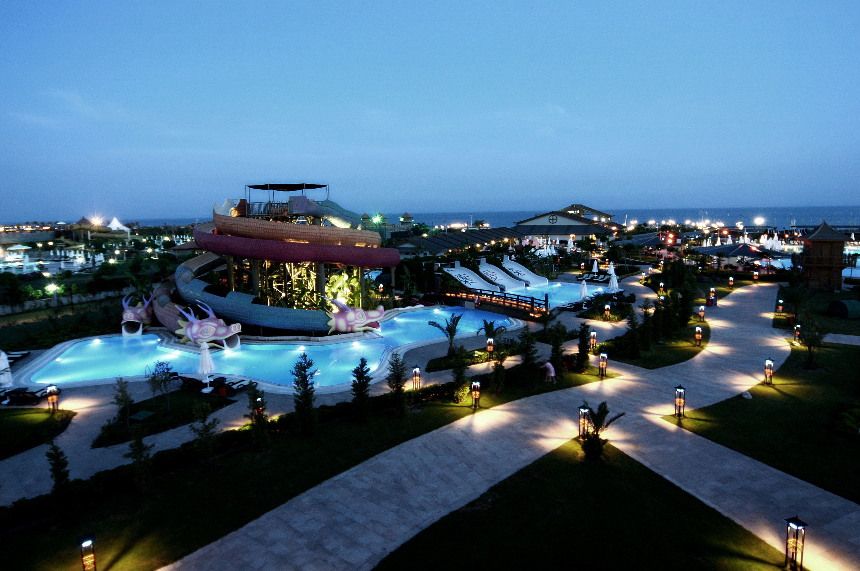 A resort with a large pool area, a water slide, and a well-lit walkway.