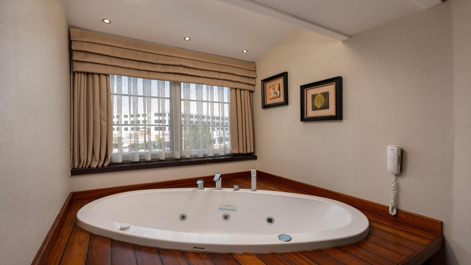 Un baño moderno con una bañera independiente, una ventana con cortinas, una obra de arte enmarcada y un teléfono.