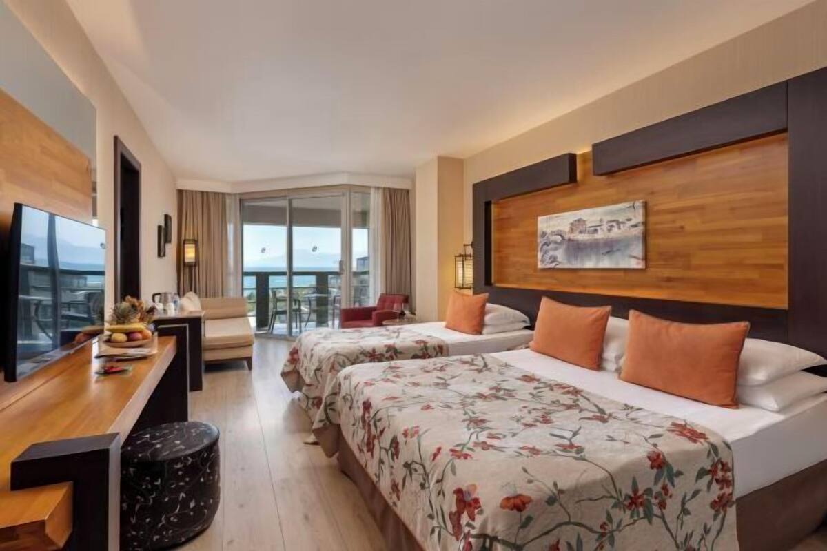 A hotel room with two beds, a desk with a laptop, a TV, and a view of the outdoors.