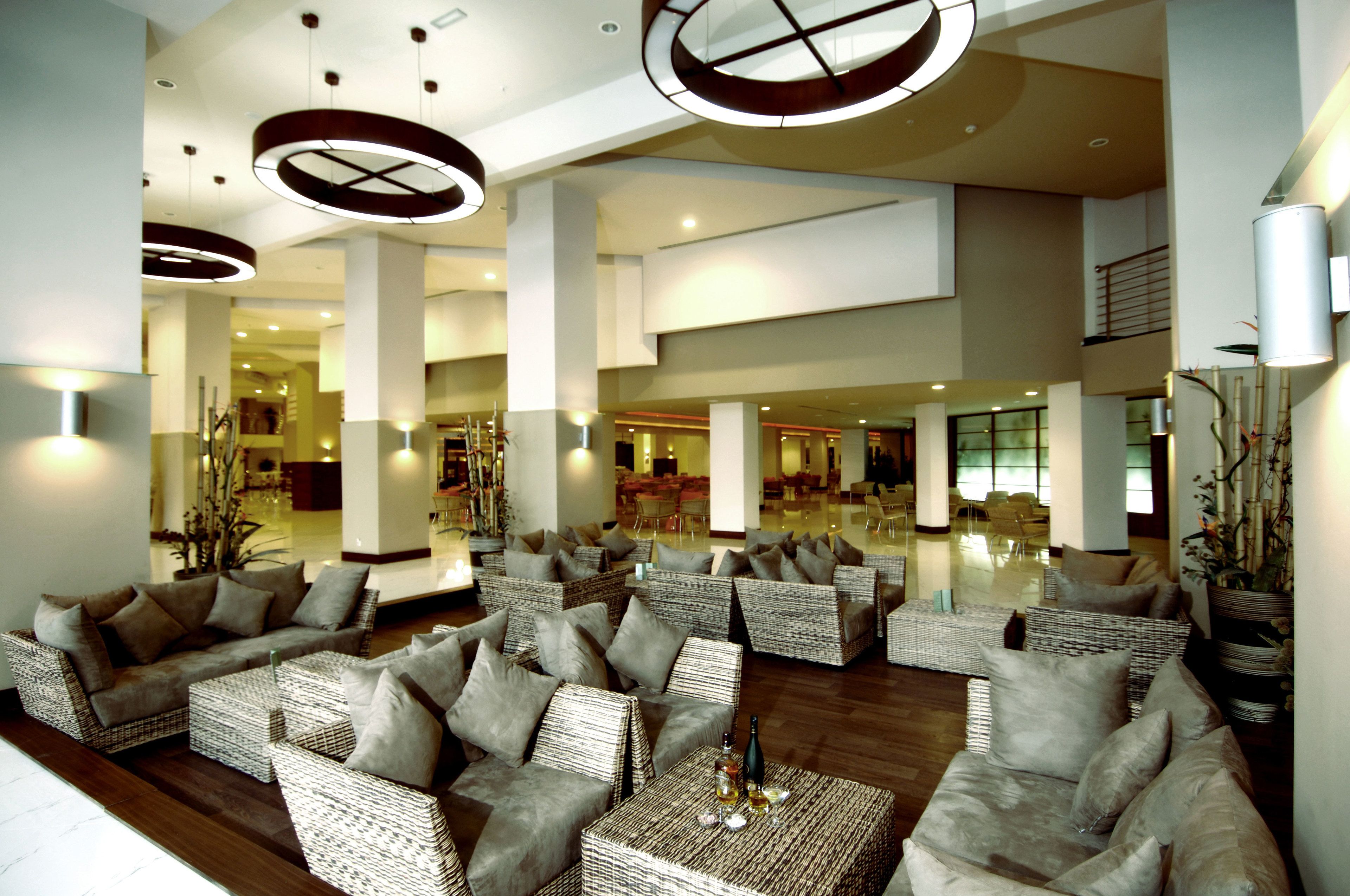 A spacious lobby with wicker furniture, large pillars, and a modern ceiling design.