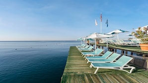 Un muelle de madera con sillas de descanso y sombrillas, con vista a aguas marinas tranquilas.