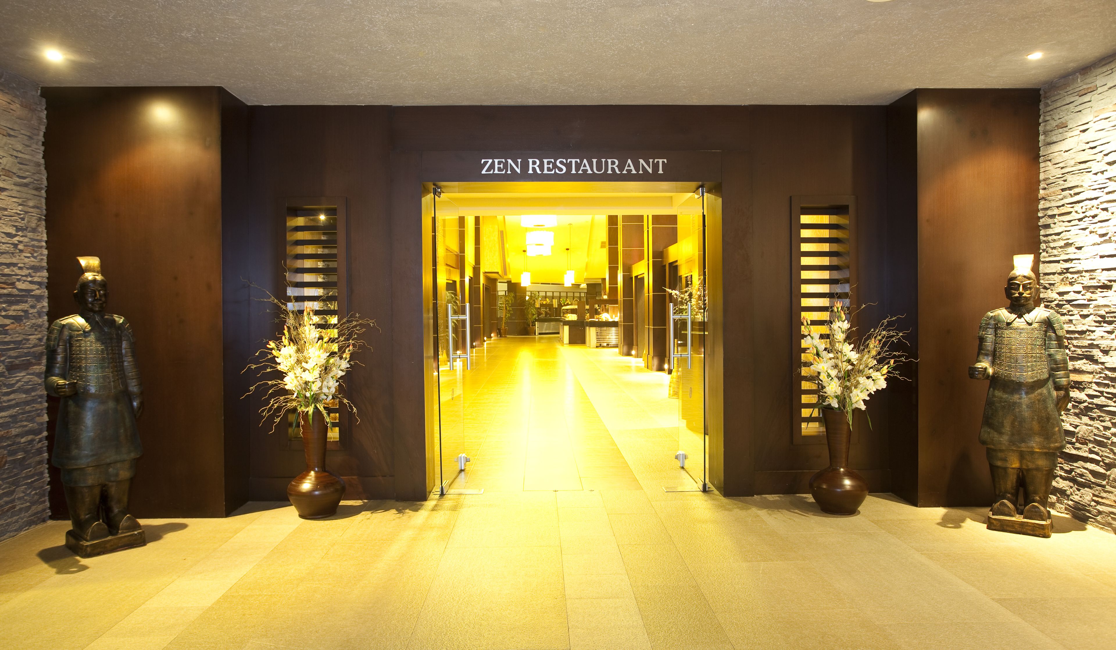 A Zen Restaurant entrance with a stone wall and two statues on either side.