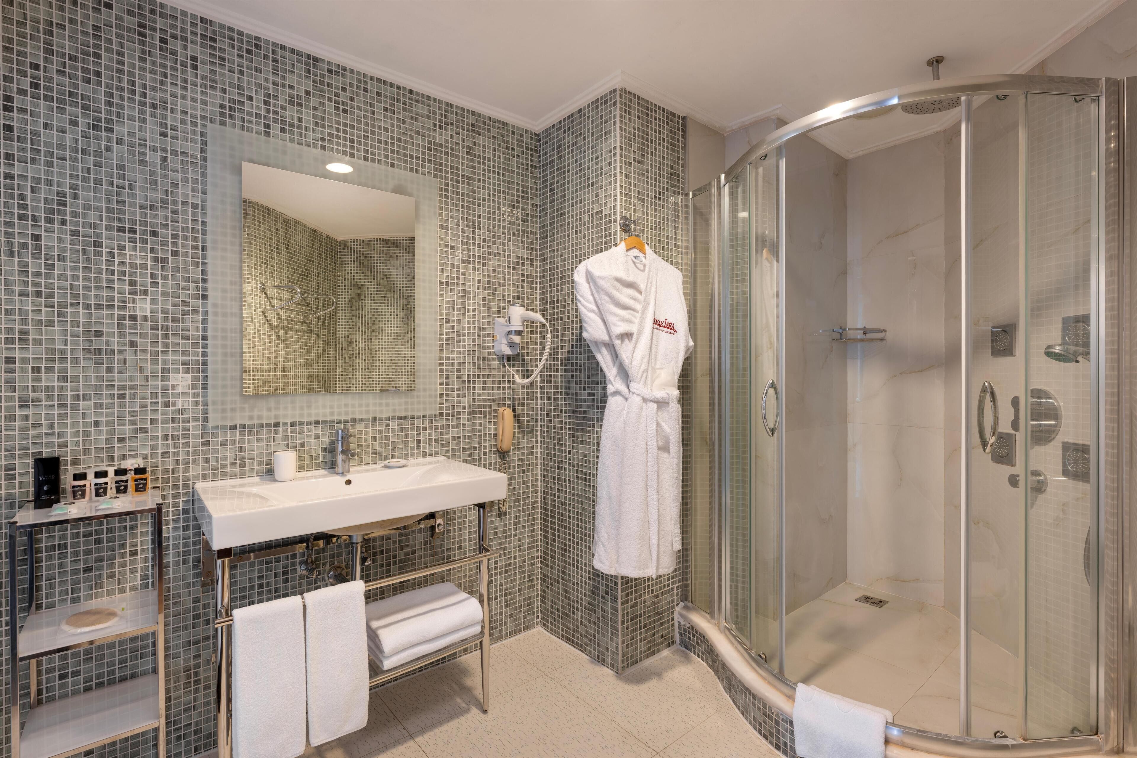 Un baño moderno con ducha de vidrio, un espejo grande y tocador con lavamanos y perchero para toallas.