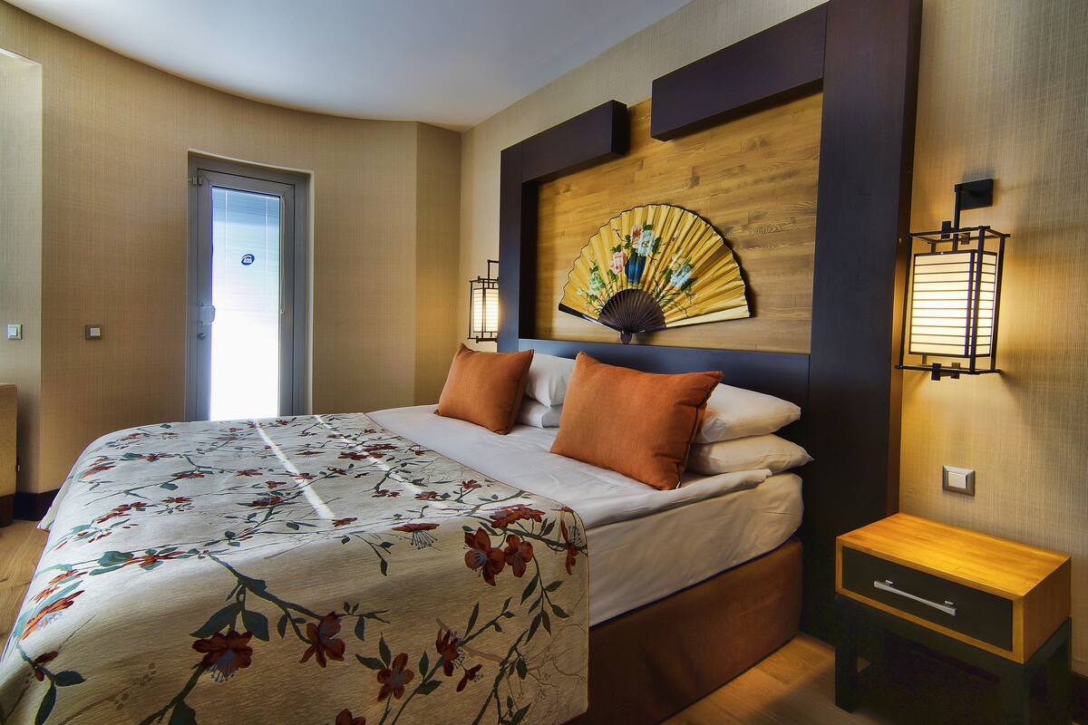 A hotel room with a bed, a wooden headboard, a nightstand, and a wall-mounted fan.