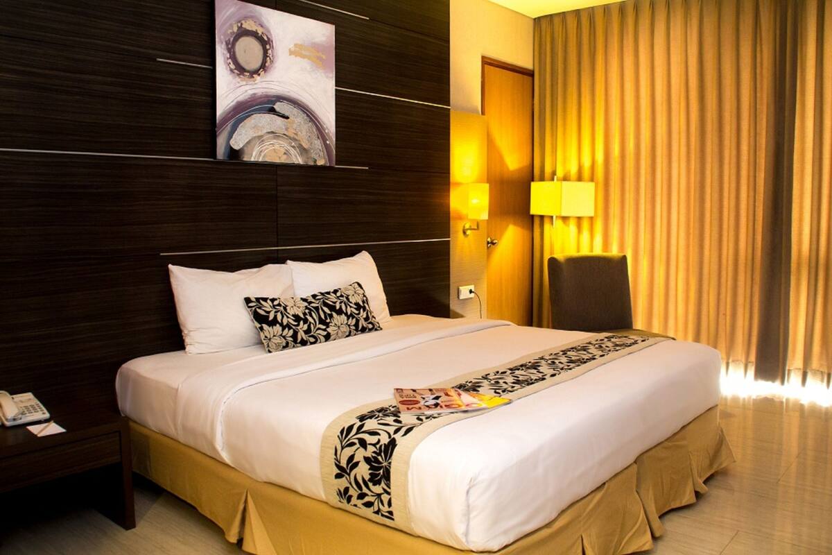 Ein Hotelzimmer mit einem großen Bett, einem Nachttisch, einer Lampe und einem Gemälde an der Wand.