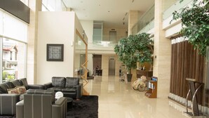 Een ruime lobby met een moderne zithoek, een grote kamerplant en een trap naar een hoger niveau.