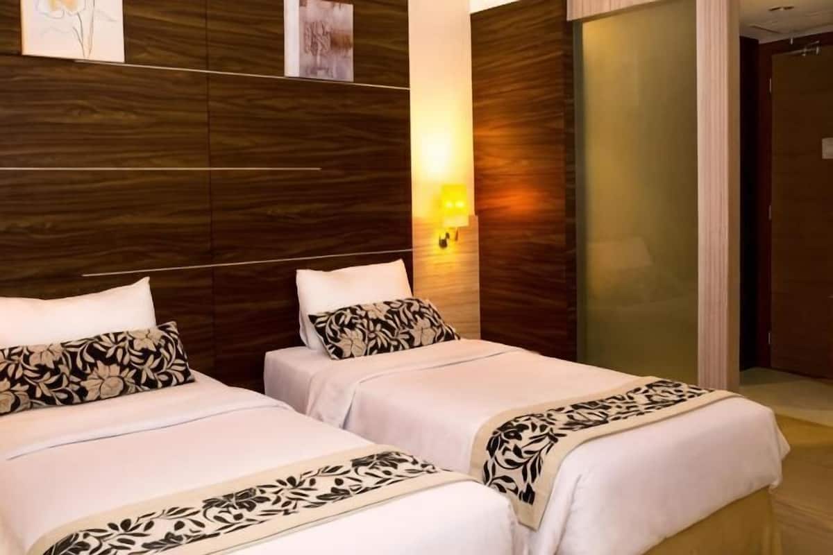 Ein Hotelzimmer mit zwei Betten, einem Holz-Kopfteil, einer Wandlampe und einer Tür mit Milchglasfenster.